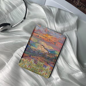 May include: A colorful landscape painting of rolling hills and a sunset sky. The painting is printed on a black e-reader case.