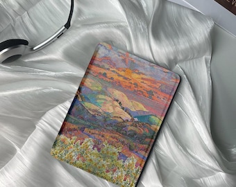 May include: A colorful landscape painting of rolling hills and a sunset sky. The painting is printed on a black e-reader case.
