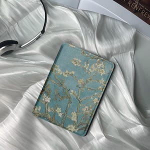 Może przedstawiać: Pokrowiec na czytnik e-booków w kolorze niebieskim i białym z obrazem kwitnącej gałęzi migdałowca. Pokrowiec wykonany jest z miękkiego, trwałego materiału i ma elegancki, nowoczesny design.