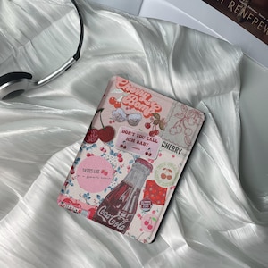 May include: Pink and white patterned Kindle cover with cherries, a Coca-Cola bottle, and the text "Cherry Bomb", "Don't You Call Him Baby", "Cherry 2018", and "Tastes Like a Summer Crush".
