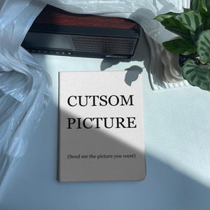 May include: A rectangular, light beige tablet case featuring the black printed text CUTSOM PICTURE and the parenthetical instruction (Send me the picture you want) centered on the front cover. The case has a smooth, matte finish.