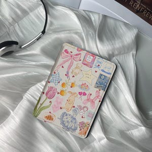 May include: A pink and white patterned e-reader cover with a variety of illustrations including a bunny, a teddy bear, a bow, and hearts. The text "You're my star!" and "Soul Mate" are visible on the cover.