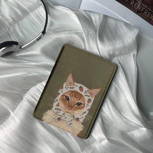 Op de afbeelding: Een groene e-reader hoes met een schattige illustratie van een kat die een witte en roze bloemenkap met aardbeien draagt. De kat heeft oranje vacht en groene ogen.