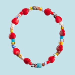 May include: A red heart-shaped beaded bracelet with colorful glass beads. The bracelet is made of red, blue, yellow, white, and green beads.