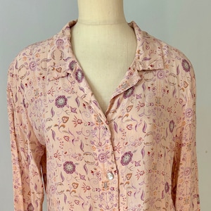 May include: A long-sleeved, button-up shirt with a pink background and a floral pattern in shades of purple, orange, and brown.