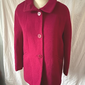 May include: A magenta-colored coat with a ribbed texture. The coat features a large collar, three matching buttons, and two front pockets. The coat is displayed on a mannequin.