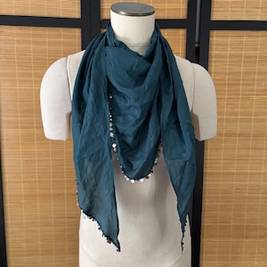 May include: A teal scarf with a triangular shape, draped on a mannequin. The scarf is adorned with silver sequins along the edges. The fabric appears lightweight and flowing, suitable for accessorizing.