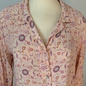 May include: A long-sleeved button-up shirt with a pink background and a floral pattern in shades of purple, orange, and brown.