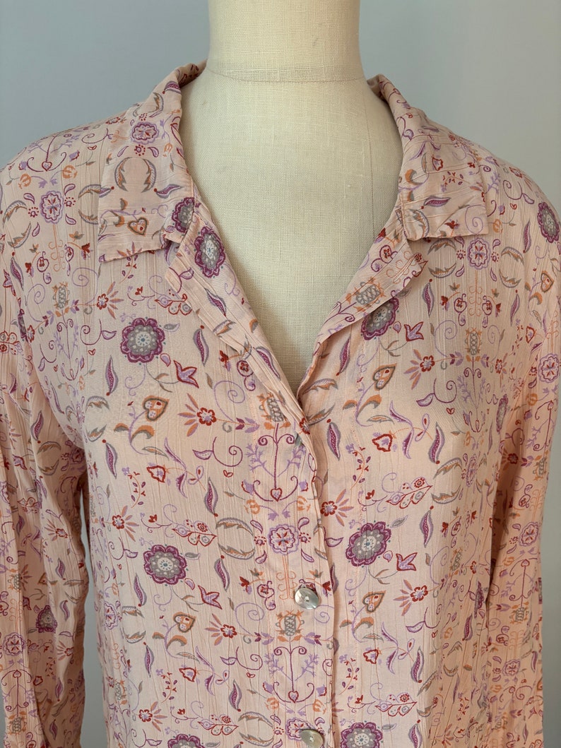 May include: A long-sleeved button-up shirt with a pink background and a floral pattern in shades of purple, orange, and brown.