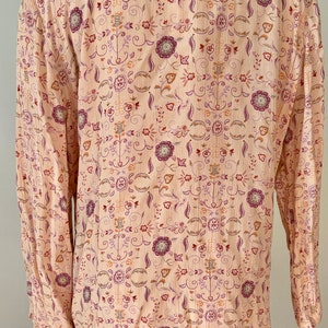 May include: A long-sleeved, light pink button-up shirt with a floral pattern in shades of purple, orange, and brown.