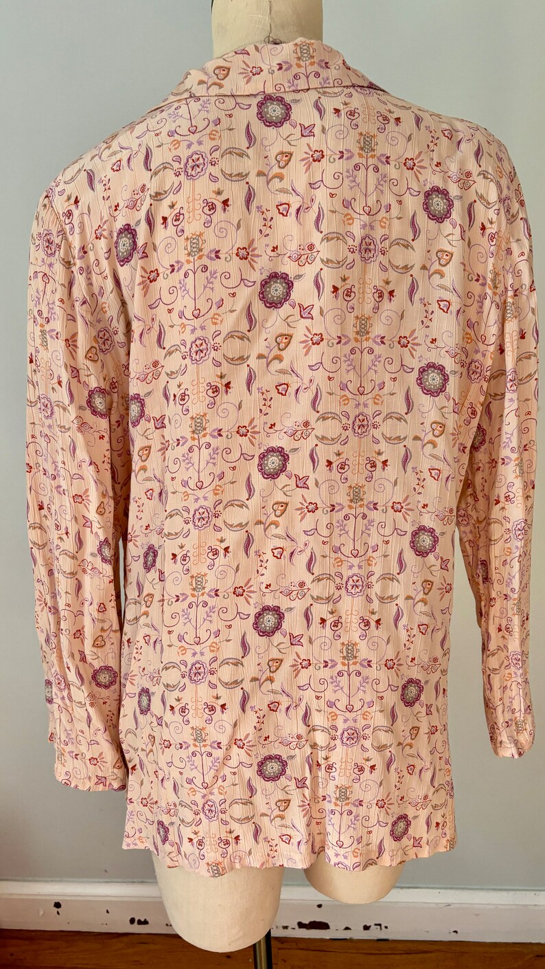 May include: A long-sleeved, light pink button-up shirt with a floral pattern in shades of purple, orange, and brown.