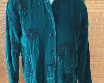 May include: A teal green velvet jacket with black embroidered floral designs. The jacket has a mandarin collar and button-down front. The long sleeves and soft fabric create a vintage look. The embroidery adds a touch of elegance to this unique garment.