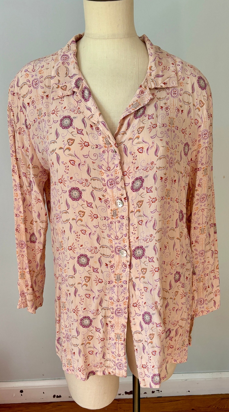 May include: A long-sleeved, button-up shirt with a pink background and a floral pattern in shades of purple, orange, and brown.