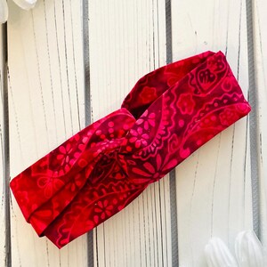 May include: A red and pink patterned fabric headband with a twisted knot design.