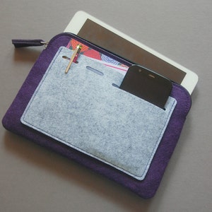 May include: A purple felt tablet case with a gray felt pocket. A tablet and smartphone are visible inside the case. A gold pen is tucked into the pocket. The case has a zipper closure.