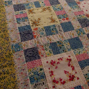 Pu&ograve; includere: Un quilt patchwork con una variet&agrave; di motivi floreali in tonalit&agrave; di blu, rosa, giallo e bianco. Il quilt &egrave; realizzato con una variet&agrave; di tessuti, tra cui fazzoletti vintage.