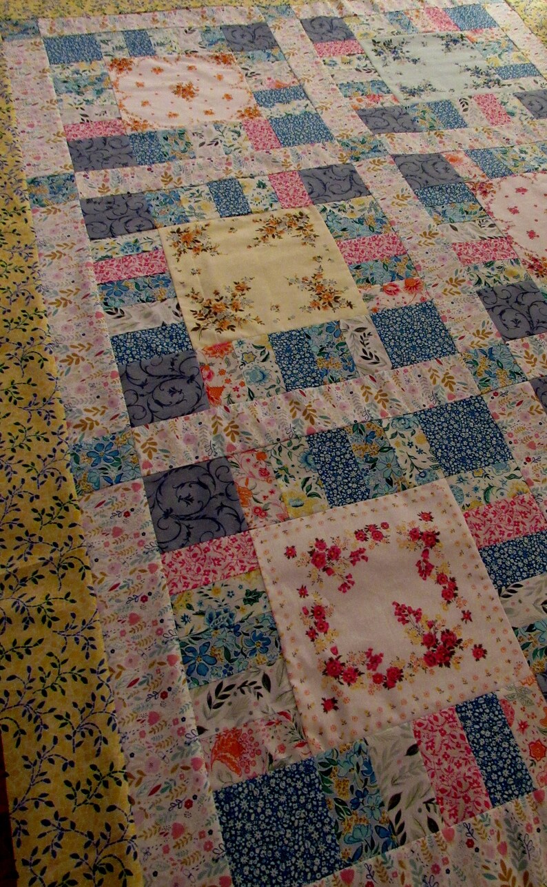 Pu&ograve; includere: Un quilt patchwork con una variet&agrave; di motivi floreali in tonalit&agrave; di blu, rosa, giallo e bianco. Il quilt &egrave; realizzato con una variet&agrave; di tessuti, tra cui fazzoletti vintage.