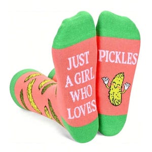 May include: Novelty socks with a pink base and green trim. The socks display the text "JUST A GIRL WHO LOVES PICKLES" and a cartoon pickle character. The design incorporates yellow pickle illustrations.