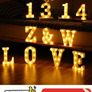 Può includere: Lettere e numeri luminosi a tendone che compongono "1314" e "LOVE" con una e commerciale. Il caldo bagliore giallo delle luci crea un'atmosfera accogliente. È visibile anche una luce decorativa a forma di cuore. È visibile anche il testo "Shopkeeper recommend".