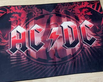 May include: A black and red rug with the band name "AC/DC" in white letters. The rug has a red and black design with a lightning bolt in the center.