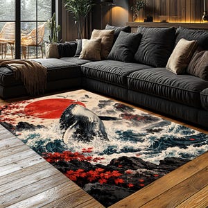 May include: A rectangular area rug featuring a graphic print of a whale breaching from ocean waves. The design includes a large red sun, dark rocky cliffs, and vibrant red maple leaves against a cream background, laid on a wooden floor.
