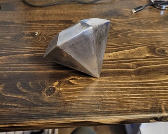 May include: A silver metal diamond-shaped sculpture on a wooden surface.