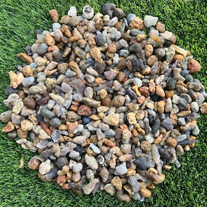 May include: A large collection of small, smooth, and textured river stones in various earthy tones including tan, brown, gray, white, and translucent amber. The stones vary in shape and size, displaying natural mineral patterns and porous surfaces.