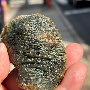 May include: A close-up of a green and brown textured rock with a rough surface. The rock has a unique, organic shape and appears to be a natural formation.