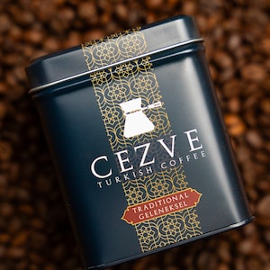 May include: A blue metal tin with gold lettering and a traditional Turkish coffee pot design. The tin says "Cezve Turkish Coffee" and "Traditional Geleneksel".