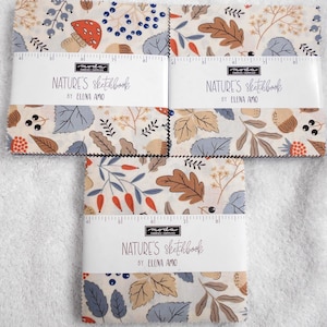 May include: Three stacks of fabric squares labeled Nature's Sketchbook by Elena Amo for Moda Fabrics. The fabric features a cream background with a botanical print of brown oak leaves, blue berries, red mushrooms, and acorns, with a visible 9-inch ruler.