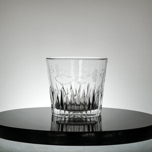Puede incluir: Un vaso de vidrio transparente con un dise&ntilde;o floral grabado en el lateral. El vaso tiene un patr&oacute;n texturizado en forma de diamante alrededor de la base.