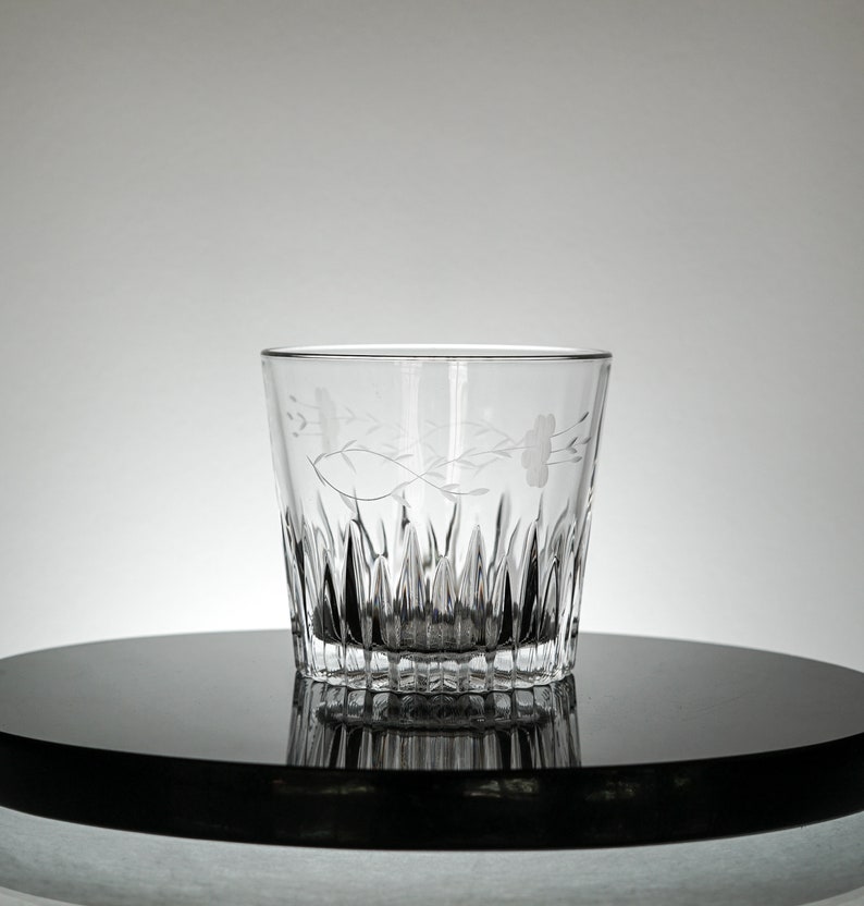 Puede incluir: Un vaso de vidrio transparente con un dise&ntilde;o floral grabado en el lateral. El vaso tiene un patr&oacute;n texturizado en forma de diamante alrededor de la base.
