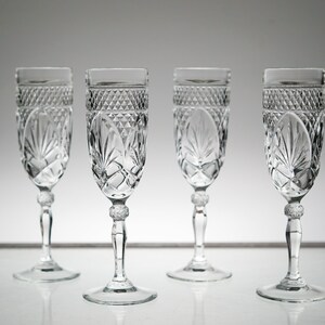 K&ouml;nnte beinhalten: Vier klare Champagnergl&auml;ser aus Glas mit geschliffenem Kristallmuster. Die Gl&auml;ser haben einen runden Boden und einen hohen, schlanken Stiel.