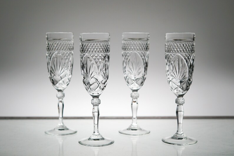 K&ouml;nnte beinhalten: Vier klare Champagnergl&auml;ser aus Glas mit geschliffenem Kristallmuster. Die Gl&auml;ser haben einen runden Boden und einen hohen, schlanken Stiel.