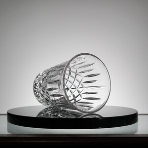 May include: A clear glass tumbler with a cut-glass design. The glass is sitting on a black circular surface.