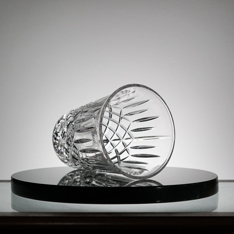 May include: A clear glass tumbler with a cut-glass design. The glass is sitting on a black circular surface.
