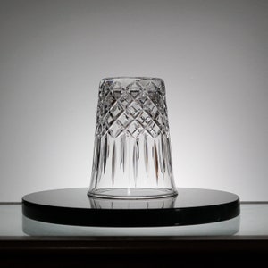 May include: A clear glass tumbler with a diamond pattern. The tumbler is sitting on a black circular surface.