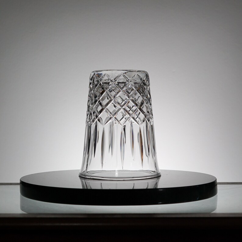 May include: A clear glass tumbler with a diamond pattern. The tumbler is sitting on a black circular surface.