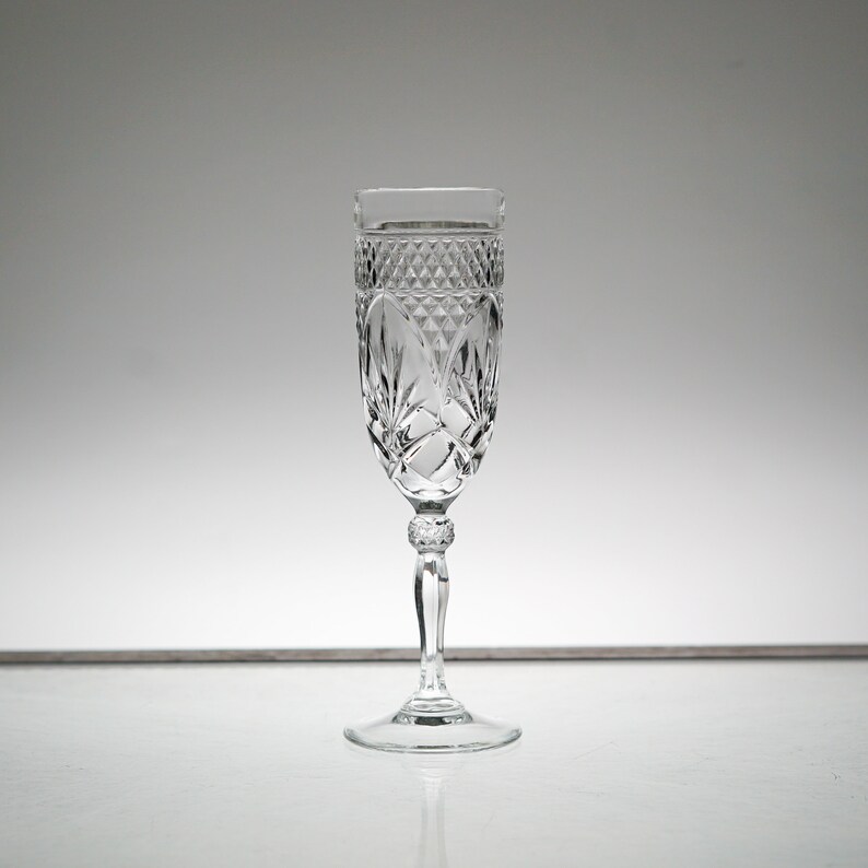K&ouml;nnte beinhalten: Eine klare Champagnerfl&ouml;te aus Glas mit geschliffenem Kristallmuster. Die Fl&ouml;te hat einen hohen, schlanken Stiel und eine breite, schalenf&ouml;rmige Oberseite.