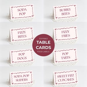 May include: A collection of editable table cards with food labels. Each card features a decorative border and text such as "Soda Pop," "Bubbly Bites," and "Fizzy Fries." The cards are displayed on white, lacy doilies.