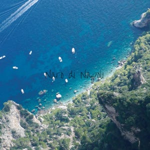Op de afbeelding: Luchtfoto van de kust van Napels, Italië, met de tekst "Naro di Napoli". De afbeelding toont een diepblauwe zee met verschillende witte boten en een spoor van een boot. Weelderige groene vegetatie bedekt de kliffen.
