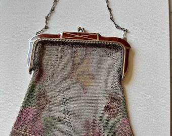 May include: An antique silver mesh purse with a decorative frame and chain handle. The frame is a reddish-brown color with silver accents. The mesh bag features a floral pattern in shades of pink, green, and yellow.