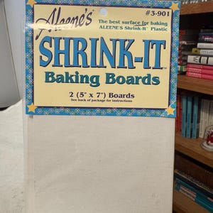 May include: A package of Aleene's Shrink-It Baking Boards. The package has a blue and yellow border with the text "SHRINK-IT Baking Boards". It contains two 5" x 7" boards. The product is designed for baking.