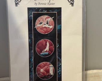 May include: A craft pattern for a seascape quilt featuring three circular designs with a seagull, sailboat, and lighthouse. The pattern is titled "Seascape" by Bonnie Kaster and "Sweet Memories".