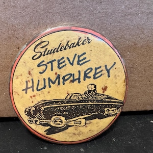 Könnte beinhalten: Ein runder Ansteckbutton mit gelbem Hintergrund und einem dünnen roten Rand. Der Text lautet Studebaker STEVE HUMPHREY in schwarzer Schreibschrift und Blockbuchstaben. Unter dem Text befindet sich eine schwarze Grafik eines Cabriolets mit Fahrer.