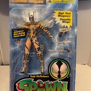 May include: Cosmic Angela action figure in a clear plastic package. The figure is gold and black with silver wings and includes high-tech weaponry. The packaging features the Spawn logo and the text "Ultra-Action Figures."