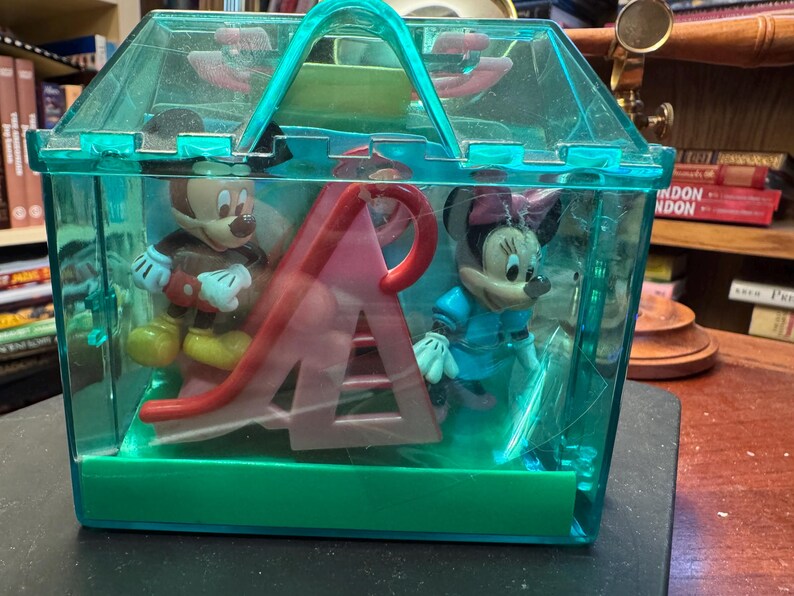 May include: A clear, turquoise plastic carrying case containing Mickey Mouse and Minnie Mouse figurines, along with a red and pink slide. Mickey is wearing brown shorts and Minnie is in a blue dress.