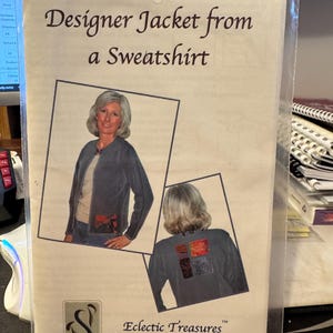 May include: A sewing pattern for a jacket made from a sweatshirt. The pattern shows a woman wearing a blue jacket and a close-up of the back of a sweatshirt with colorful fabric patches. The pattern is titled "Designer Jacket from a Sweatshirt" and is from "Eclectic Treasures" by "The Sewing Place".