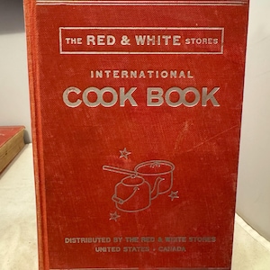 以下が含まれることがあります： 「International Cook Book」と題された、The Red & White Storesのヴィンテージの赤い料理本。表紙には銀色の文字と、鍋や星のイラストが描かれています。アメリカとカナダで販売されています。