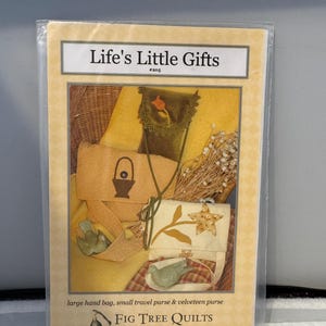 May include: A package featuring a design for a large hand bag, small travel purse, and velveteen purse. The package has the text "Life's Little Gifts" and "Fig Tree Quilts". The image shows the finished products in shades of tan, green, and cream.